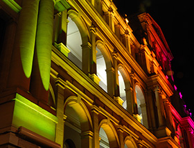 Building at night lit up by green, red and yellow spotlights