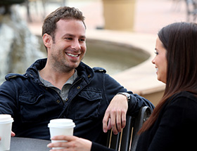 Man smiling and drinking coffee with a woman