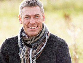 A man standing in a field, wearing a scarf and smiling
