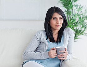 A contemplative woman holding a cup of tea whilst sitting on the sofa