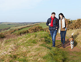 smiling couple walk dog in countryside